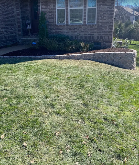 Curved stacked stone retaining wall with fresh mulch beds along a brick home