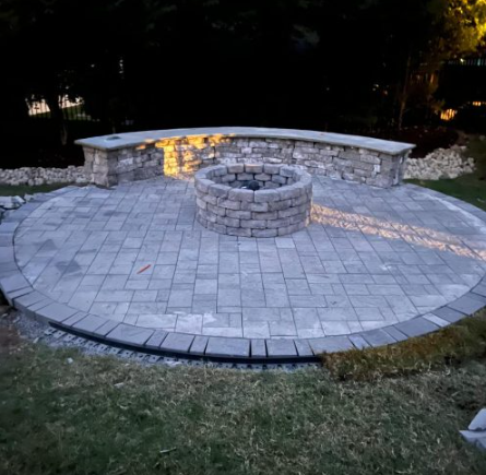 Paver fire pit patio with seat wall lit at dusk
